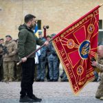 Ukraine's President Volodymyr Zelensky holding a flag insignia as a serviceman pays his respect during a ceremony marking Defenders' Day, a holiday honoring veterans and fallen members of the Ukrainian armed forces, in Kyiv, Ukraine. (Ukrainian Presidential Press Service)